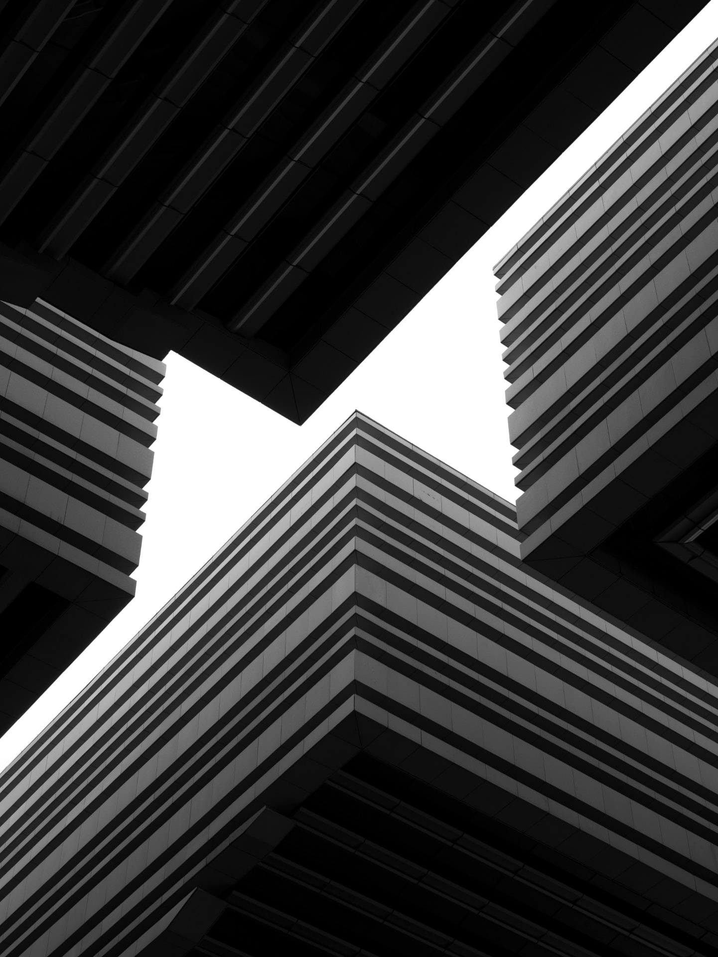Monochrome angular towers with striped facades framing a bright opening to the sky