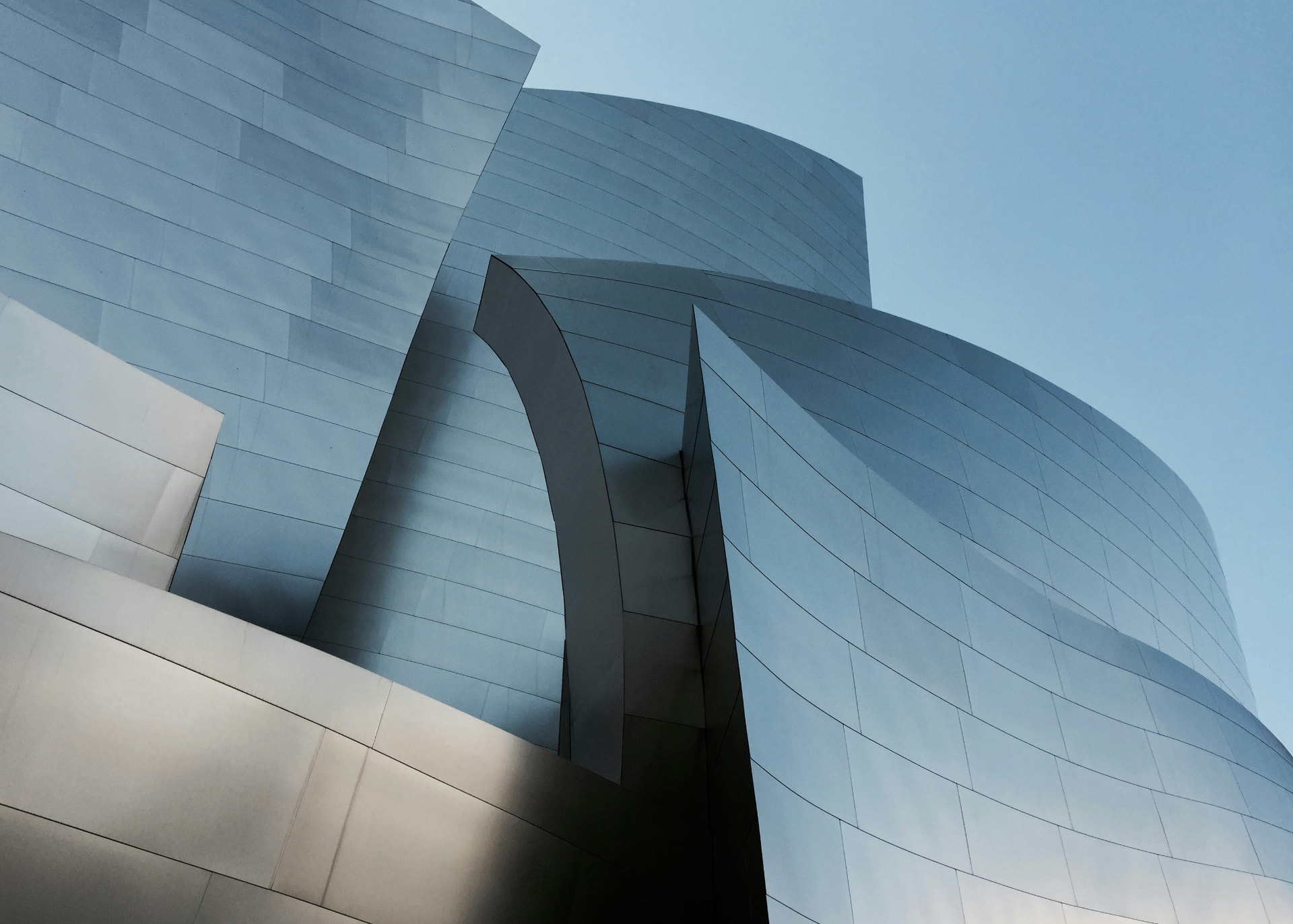 Sculptural silver-clad architectural volumes curving beneath pale blue sky