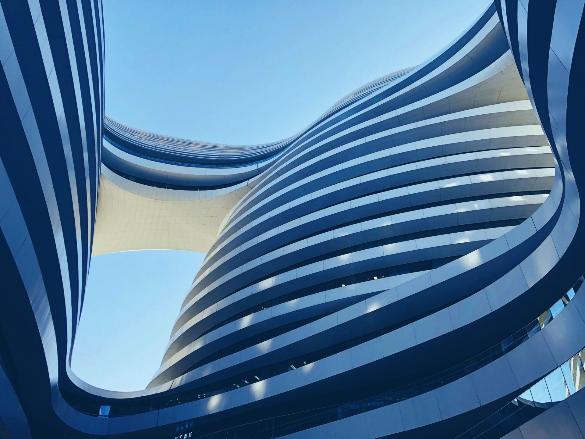 Curved blue-grey buildings joined by a sweeping elevated bridge beneath clear blue sky